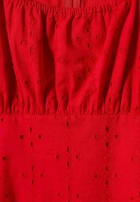 Tissu rouge avec des motifs brodés, présentant de petits trous et des motifs floraux. Texture froncée en haut, moitié inférieure lisse.