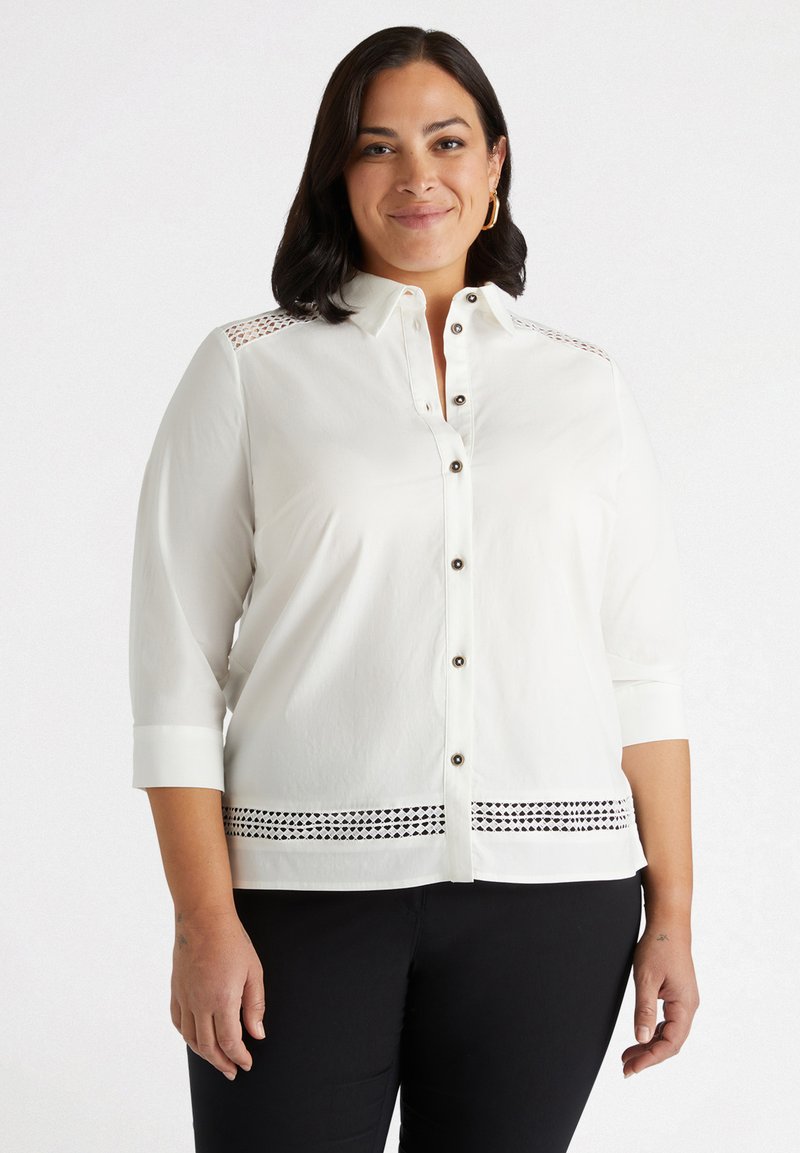 Camicia bianca con maniche a tre quarti, caratterizzata da dettagli in pizzo sulle spalle e un motivo decorativo a intaglio sull'orlo.