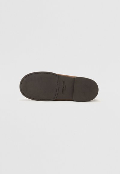 Brown suede footwear with a smooth, rounded toe and a contrasting rubber sole. Features embossed logo on the side. Flat design.