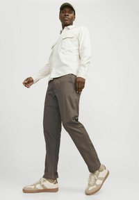 Lässiges Outfit mit einem hellen Hemd mit Knopfleiste und zwei Brusttaschen, braunen Hosen und beigen Sneakern mit cremefarbenen Akzenten.
