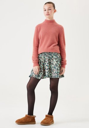 Flauschiger pinker Rollkragenpullover, gemusterter mintgrüner Rock, schwarze Strumpfhose und braune Wildleder-Stiefeletten mit Futter aus Fell und flachen Sohlen.