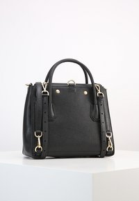 Sac à main en cuir noir texturé avec deux poignées supérieures, bandoulière amovible et ferrures métalliques dorées, présenté sur une surface blanche.