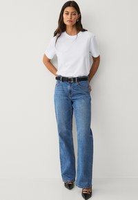 Camiseta de algodón blanca, jeans de mezclilla anchos y azules, cinturón de cuero negro con hebilla plateada, tacones de punta negra, estilo minimalista.