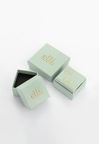 Mintgrønne emballagebokse med en mat overflade. Én åben boks afslører et sort interiør. Guldtekst branding på overfladerne.