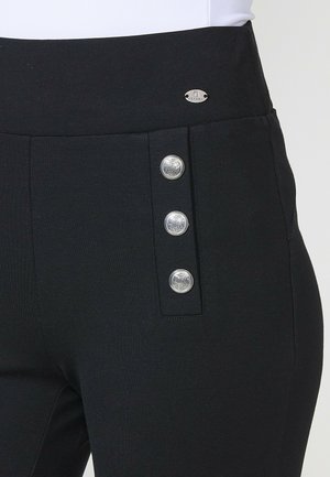 Pantaloni negri cu croi ajustat, având o textură netedă, cu o talie înaltă și trei nasturi metalici pe partea stângă. Emblema argintie a mărcii este vizibilă.