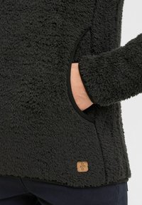Pullover in pile nero con materiale texturizzato e soffice, dotato di tasca laterale e piccolo logo in pelle vicino all'orlo.