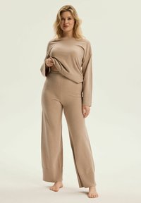 Beżowy zestaw do wypoczynku z dzianiny, składający się z krótkiego długiego rękawa i spodni typu wide-leg, charakteryzujący się miękką fakturą i luźnym krojem.