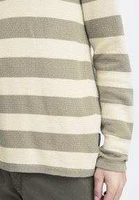 Stripete genser i kremfarge og olivengrønn, strikket tekstur med lange ermer og rund hals, med detalj av sideetikett.