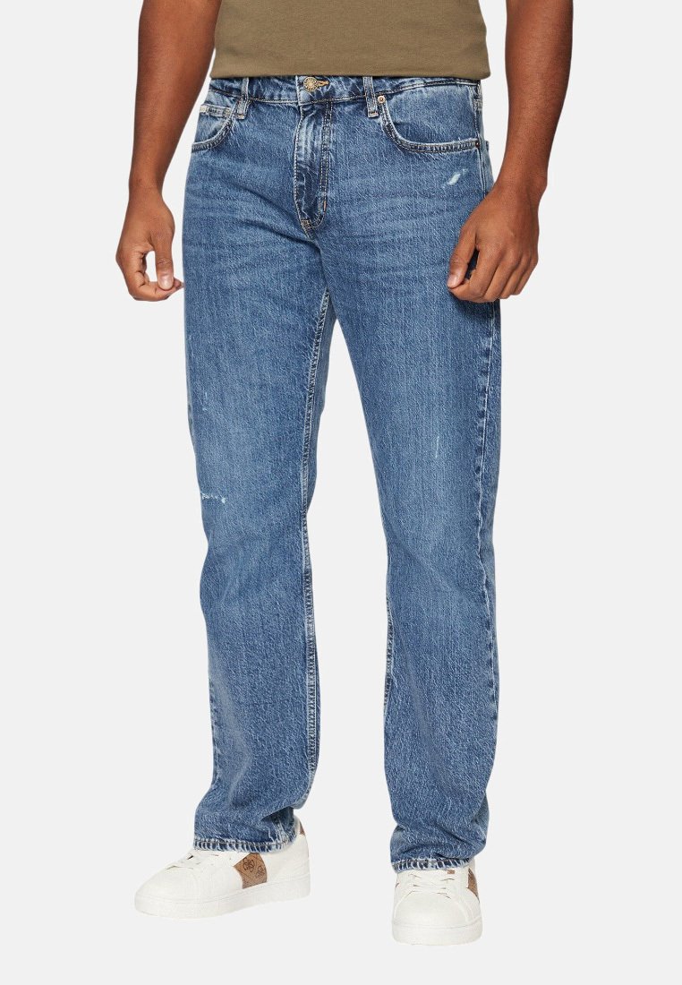 Jeans in denim blu con taglio dritto, caratterizzati da lievi rotture, cinque tasche e chiusura a bottoni. Indossati con sneaker bianche.