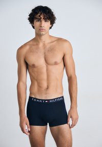 Boxeurs noirs avec une ceinture logo arborant "TOMMY HILFIGER." Tissu lisse, design ajusté et longueur mi-cuisse.