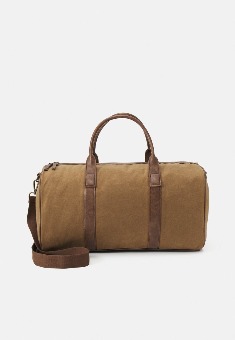 Sac de sport en toile marron avec des accents en cuir, doté de doubles poignées, d'une bandoulière amovible et d'une fermeture éclair.