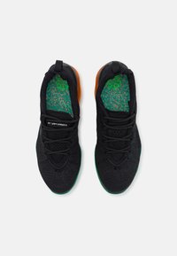 Black athletic shoes with a textured knit upper, green accent on the sole, and orange heel. Features laces and an insole with a green speckled pattern.