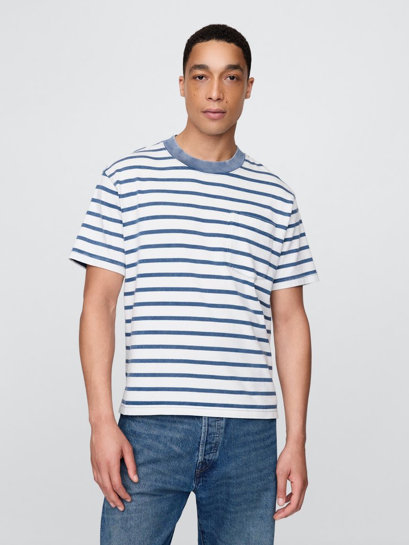 Camiseta de algodón rayada con franjas horizontales azules y blancas, escote redondo, mangas cortas y un bolsillo en el pecho. Combinada con unos vaqueros azules.