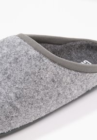 Šedá plyšová nazouvací bota s měkkou texturou, zaobleným designem a šedým textilním lemem. Podešev je plochá a hladká. Bez viditelných vzorů nebo akcentů.