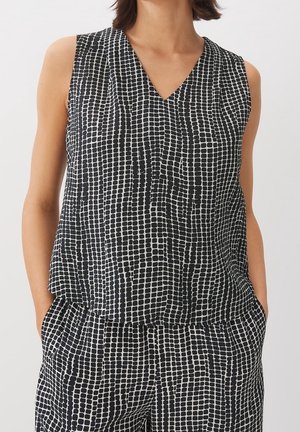 Haut sans manches noir et blanc à motifs et pantalon assorti portés par une personne debout, les mains dans les poches.