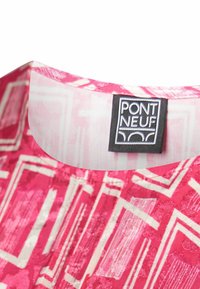 Tissu à motifs roses et blancs avec des formes géométriques et une étiquette noire indiquant "PONT NEUF" cousue à l'intérieur de l'encolure.