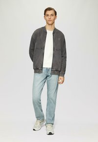 Chaqueta bomber gris con cremallera frontal, puños elásticos y dos bolsillos frontales, combinada con jeans de color azul claro y zapatillas grises. Diseño simple.