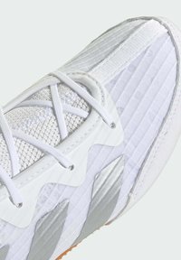 Valkoinen urheilukenkä, jossa on teksturoitu verkkomateriaali päällisosassa, heijastavia hopeisia yksityiskohtia ja kumipohja. Nauhat ovat valkoiset ja risteävässä kuviossa.