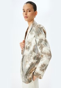 Lettern blazer i beige og brun tie-dye-mønster, med reverskrave, to lommer og en afslappet pasform med let faldende skuldre.