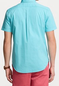 Kortärmad skjorta i ljusblå bomull, med en veck bak, rundad nederdel och krage. Buren med rosa shorts och ett brunt armbandsur.