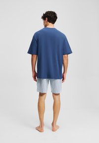 Camicia azzurra a maniche corte abbinata a pantaloni corti a righe bianche e blu navy. Tessuto morbido, vestibilità rilassata e orlo che termina appena sopra il ginocchio.