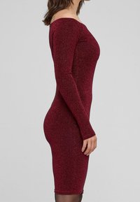 Robe bodycon bordeaux à manches longues, en tissu texturé et pailleté, au design ajusté mettant en valeur la silhouette.