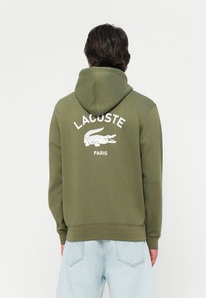 Felpa con cappuccio verde oliva con testo "LACOSTE" bianco e logo coccodrillo sul retro, realizzata in tessuto morbido e testurizzato.
