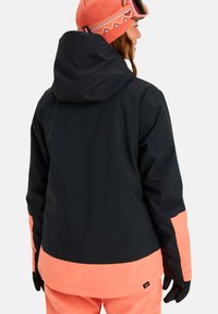 Jachetă de schi neagră și coraliu cu glugă, blocuri de culoare contrastante la tiv și mâneci, textură netedă, proiectată pentru uz exterior.