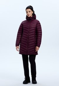 Bordeaux pufferjack met een capuchon, voorzien van een ritssluiting aan de voorkant en zijzakken, een gewatteerd ontwerp en een iets langere snit voor extra warmte.