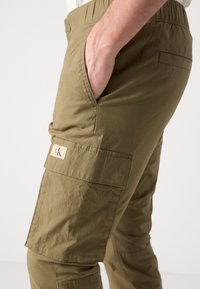 Olijfgroene cargobroek, met een verstelbare tailleband, zijzakken en een CK-logo patch, gemaakt van duurzame, gestructureerde stof.