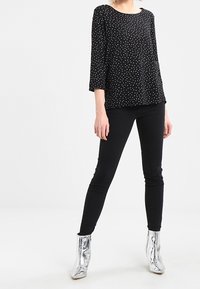 Top negro con lunares, de mangas tres cuartos, combinado con jeans negros ajustados y botines metálicos plateados. Diseño sencillo y moderno.