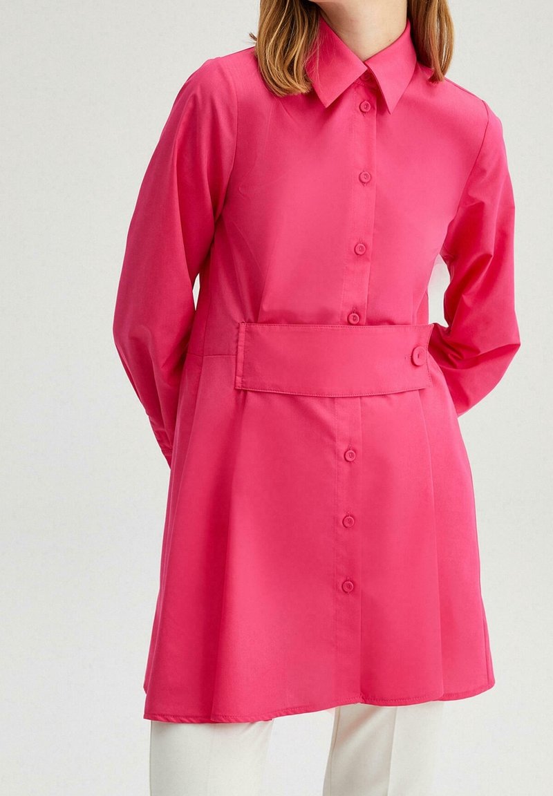 Túnica de manga larga de color rosa brillante con un frente de botones y cuello. Cuenta con una cintura ceñida y una textura de tela suave.