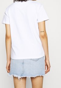 Biała bawełniana koszulka z krótkim rękawem, połączona z jasnobłękitną dżinsową spódnicą o postrzępionym wykończeniu i detalach na tylnej kieszeni.
