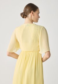 Yellow chiffon dress featuring a soft, flowing design, short flutter sleeves, and a gathered waistline for a relaxed fit.