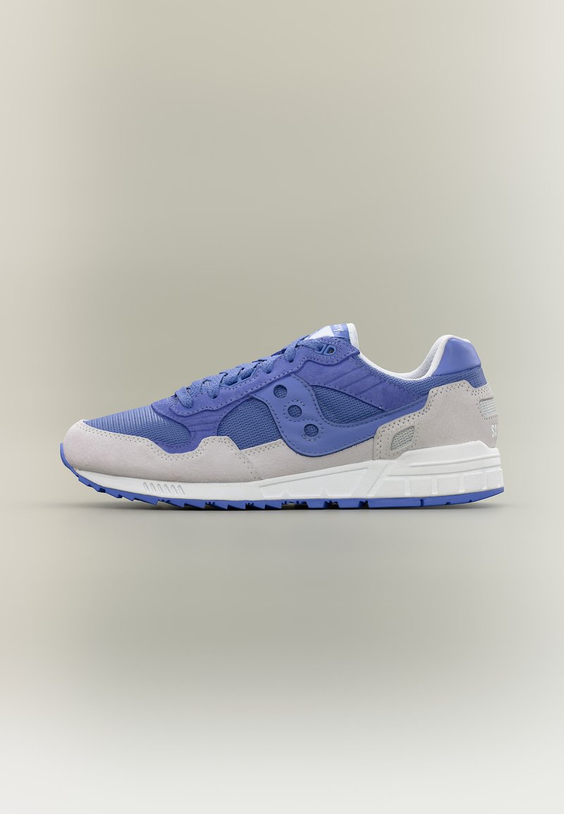 Αθλητικό παπούτσι με χαμηλό προφίλ, μπλε πλέγμα και επάνω μέρος από σουέντ, μπεζ επιφάνειες από σουέντ, λευκή μεσαία σόλα και μπλε λαστιχένια εξωτερική σόλα, εμφανιζόμενο σε πλάγια αριστερή όψη.