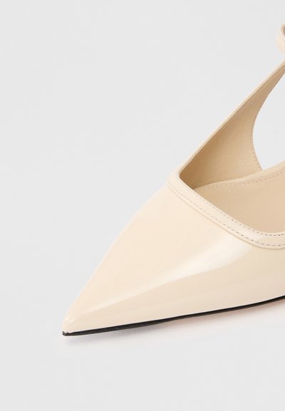 Μπεζ παπούτσι με λάκα και μυτερή μύτη, λεπτό λουρί και λεία υφή. Διαθέτει χαμηλή κοπή στο επάνω μέρος και μαύρη σόλα.