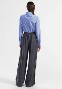 Camicia a righe blu e bianche con colletto button-down, abbinata a pantaloni grigi larghi con vita elasticizzata e strisce laterali in contrasto.