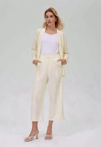 Κρεμ tailored σακάκι και παντελόνι σε χαλαρή γραμμή, συνδυασμένο με λευκό τοπ. Έχει λεία υφή και μινιμαλιστικό σχέδιο. Σανδάλια με τακούνι.