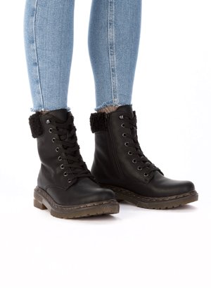 Schwarze Leder-Stiefeletten mit Schnürung, seitlichem Reißverschluss und Fellfutter am Schaft; robuste Sohle und strukturierte Oberfläche. Jeans mit fransigem Saum sichtbar.