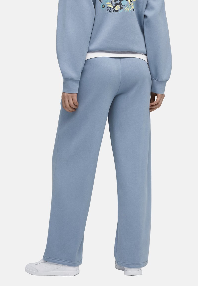 Pantalones de chándal azul claro hechos de tela suave, con un diseño de pierna recta y cintura elástica. Combinados con zapatillas blancas.