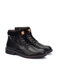Botas de cuero negro hasta el tobillo con puntera redonda, cordones en la parte delantera y suela roja en contraste. Presentan un detalle de hebilla en el lateral y un forro interior suave.