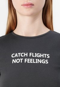 Dark gray t-shirt with short sleeves, featuring bold white text that reads "CATCH FLIGHTS NOT FEELINGS" across the chest.