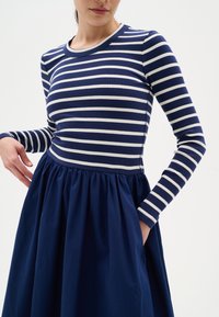 Robe à manches longues avec un corsage ajusté à rayures bleu marine et blanc, passant à une jupe bleu marine ample et froncée avec poches.