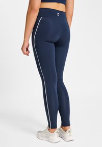 Marinblå legging med hög midja och vita sidostripe, tillverkade av stretchigt tyg med slät textur och utan synliga mönster.