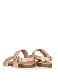 Sandalias de color rosa pálido con parte superior de cuero brillante, hebilla ajustable y suela de corcho. Diseño plano con punta abierta y correas para el tobillo.