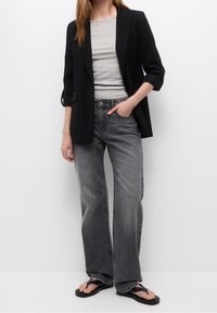 Czarna marynarka, szary prążkowany top i szare szerokie spodnie typu high-waist. Uzupełnione czarnymi klapkami. Prosty design, casualowe tekstury materiałów.