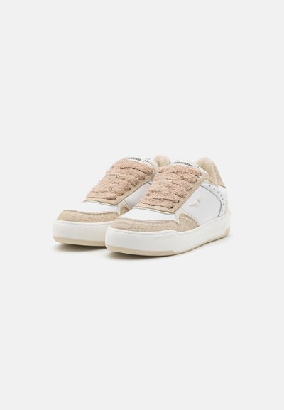 White sneakers with beige textured upper, plush fabric tongue, and embossed accents. Rubber sole with a woven pattern and logo detail.