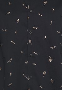 Granatowa koszula zapinana na guziki, z rozproszonymi małymi, beżowymi kwiatowymi nadrukami i czarnymi guzikami na środku.