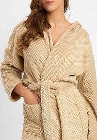 Beżowy szlafrok wykonany z teksturowanej tkaniny. Posiada kaptur, kopertowy krój oraz dopasowany pasek do wiązania. Wyposażony w przednie kieszenie dla wygody.