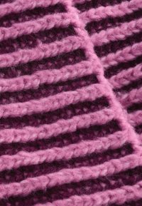 Stickad tyg i nyanser av rosa och djup lila, med tjocka, strukturerade ränder och växlande färgband som skapar en lagerliknande effekt.